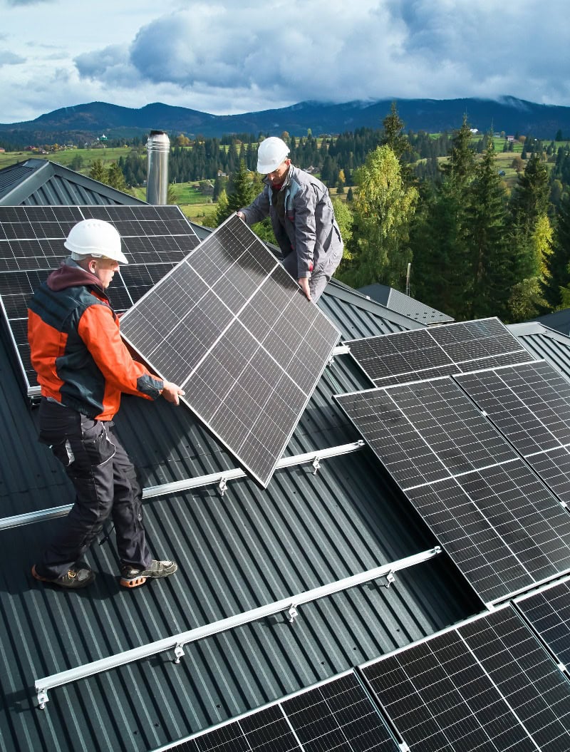 Techniker tragen Photovoltaik-Solarmodule bei der Installation einer Solaranlage auf dem Dach eines Hauses